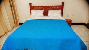Cama com colcha azul, cabeceira de madeira e dois travesseiros.