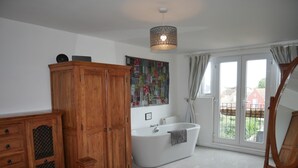 A bedroom with a large bed, a wooden wardrobe, a white bathtub, and a window with curtains. - Close to beaches and town (Broadstairs)