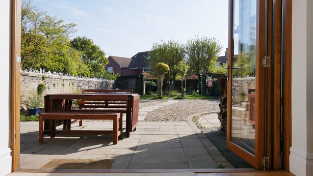 An open sliding glass door leading to a patio area with a wooden bench and a stone wall. - Close to beaches and town (Broadstairs)