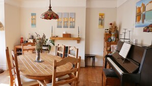 A dining area with a wooden table and chairs, a piano, and wall art. - Close to beaches and town (Broadstairs)