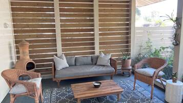 A cozy outdoor seating area with a sofa, two wicker chairs, a coffee table, and a decorative pottery piece.