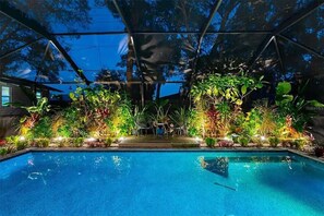 A swimming pool with a surrounding garden and a covered area with a metal roof.