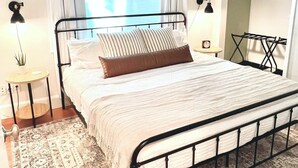 A neatly arranged bedroom with a bed, bedside lamps, a hanging light fixture, a patterned rug, and a view through a window. - Backyard Oasis & Resort Style Pool (Bradenton)