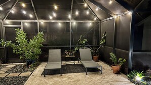 A covered outdoor seating area with two lounge chairs, potted plants, and a tiled floor. - Backyard Oasis & Resort Style Pool (Bradenton)