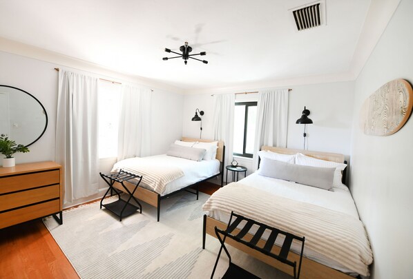 A modern bedroom with two single beds, a ceiling fan, a bedside table with a lamp, a dresser, and a large mirror.