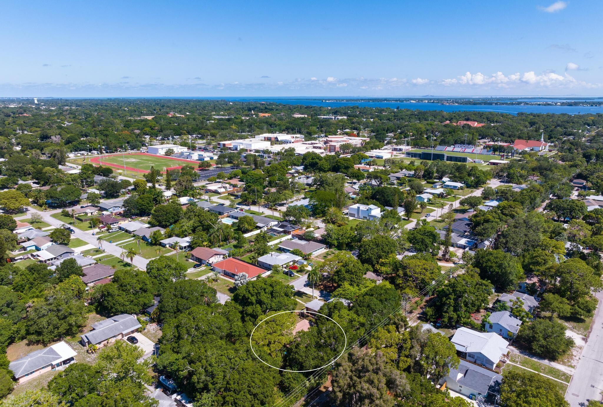 An aerial view of a residential area with houses, a sports field, and a body of water in the background.