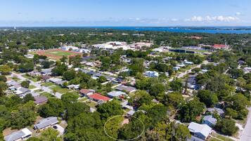 An aerial view of a residential area with houses, a sports field, and a body of water in the background.