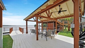 A covered outdoor deck with a view of the water, wooden furniture, and a ceiling fan.