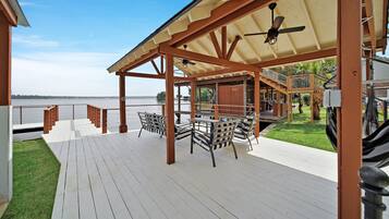 Une terrasse extérieure couverte avec vue sur l’eau, des meubles en bois et un ventilateur de plafond.