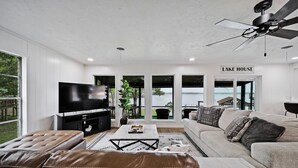 A modern living room with a large flat-screen TV, leather sofas, a coffee table, and a ceiling fan.
