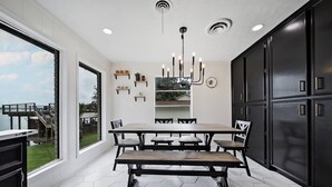 A modern kitchen with a large dining table, black cabinets, and a view of the outdoors.