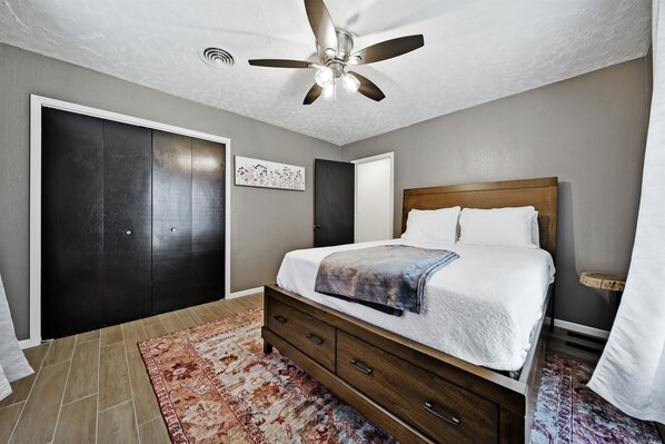 A bedroom with a bed, a ceiling fan, a dark wardrobe, and a patterned rug. - Eagle's Cove: Lake Livingston Waterfront Retreat (Trinity)