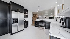 A modern kitchen with black cabinets, stainless steel appliances, a marble countertop, and a stone accent wall.