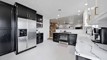 Une cuisine moderne avec des meubles noirs, des appareils en acier inoxydable, un plan de travail en marbre et un mur d’accent en pierre.