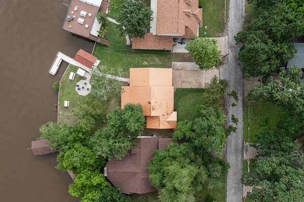 An aerial view of a residential area with a house featuring a sloped roof, a dock, and a small patio with outdoor furniture.
