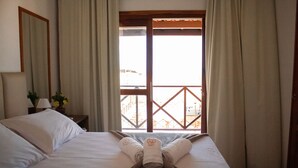 Een hotelkamer met een bed, een nachtkastje met een lamp en uitzicht op het balkon.