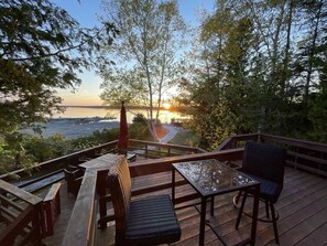 A deck with wooden furniture, overlooking a body of water and trees.