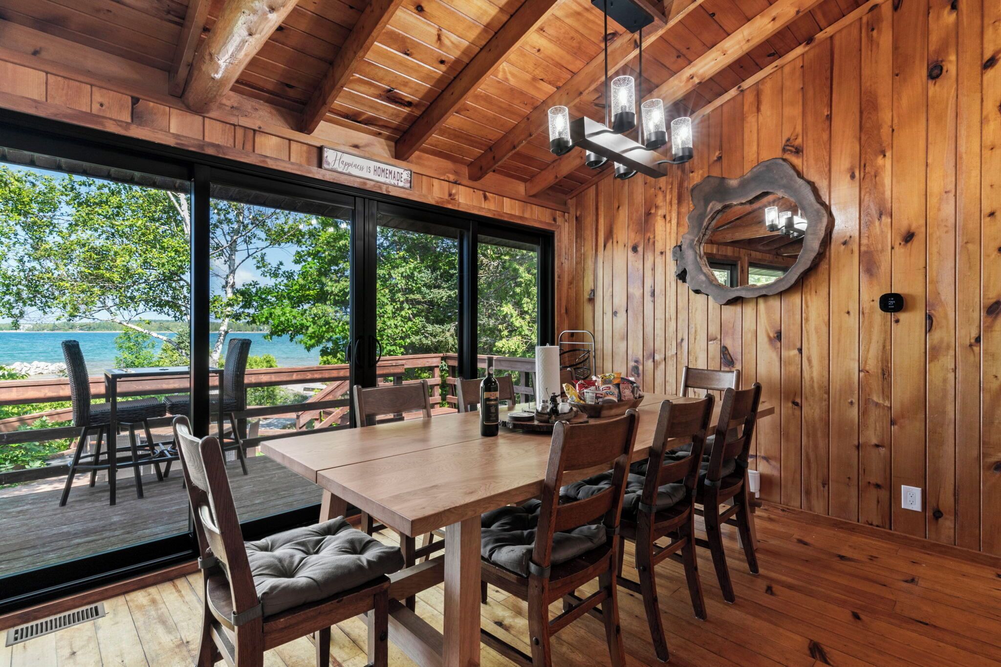A wooden deck with a table and chairs, large windows, and a view of the beach.