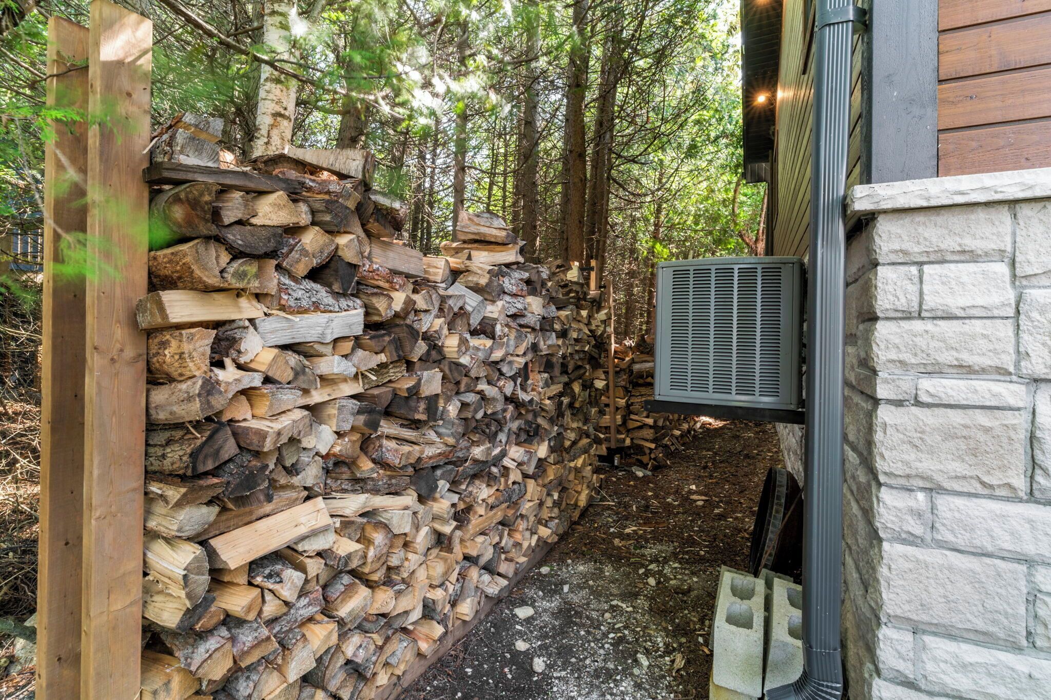 A stone wall with a stack of firewood and a metal vent.