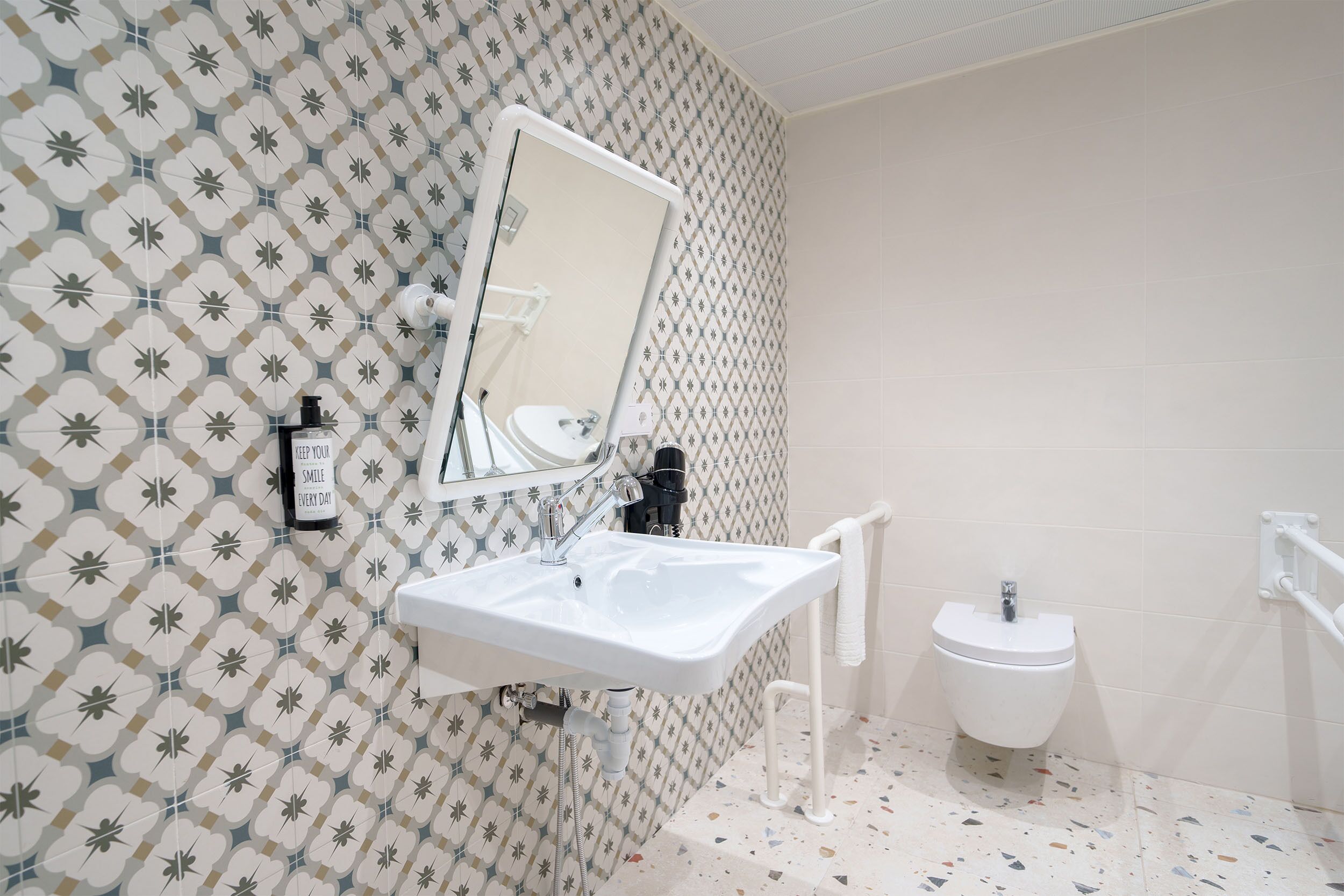 Ein Badezimmer mit strukturierter Wand, einem weißen Waschbecken, einem Spiegel, einer Toilette und einer Handstange.