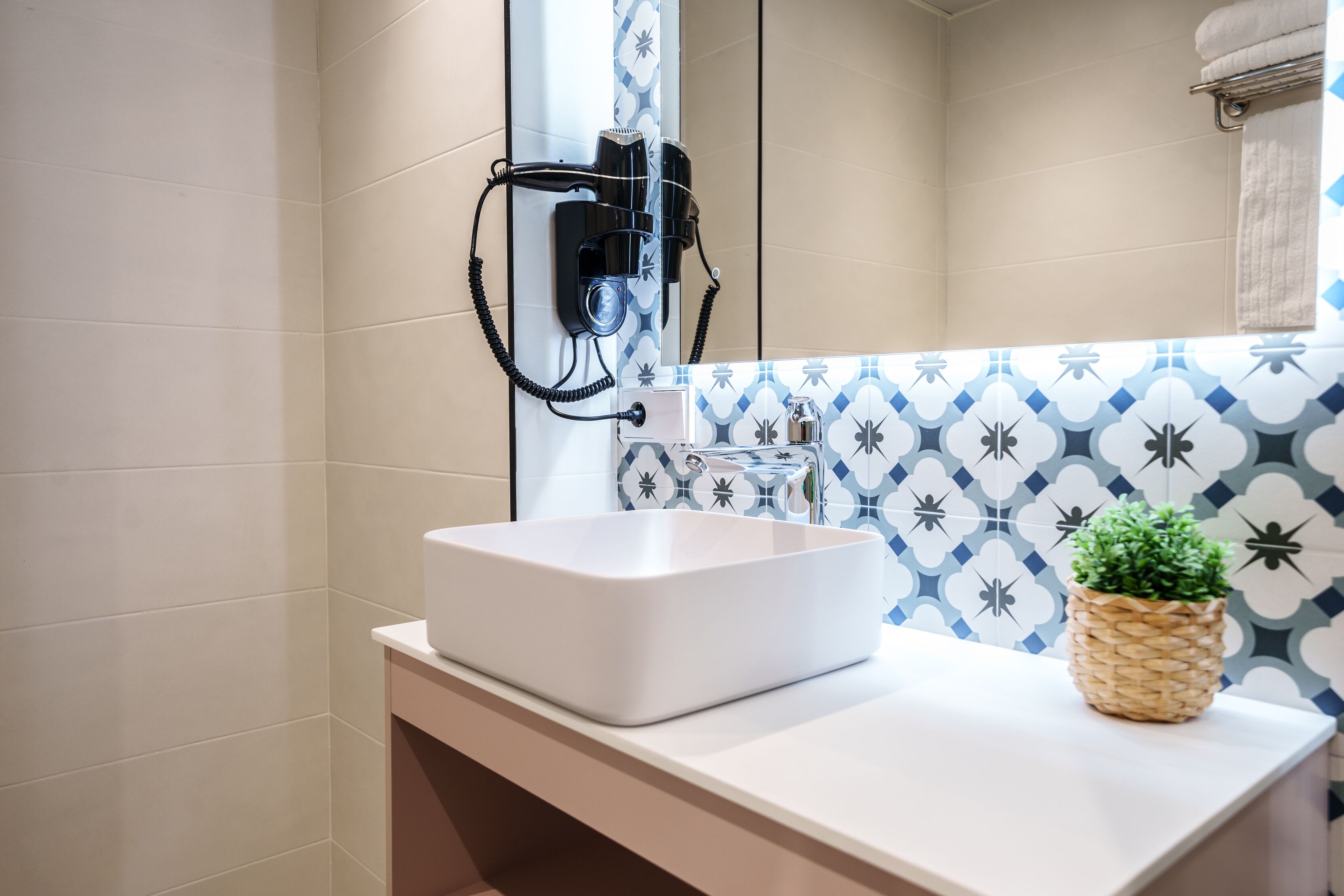 A bathroom with a white sink, a hairdryer mounted on the wall, and a patterned tile backsplash.