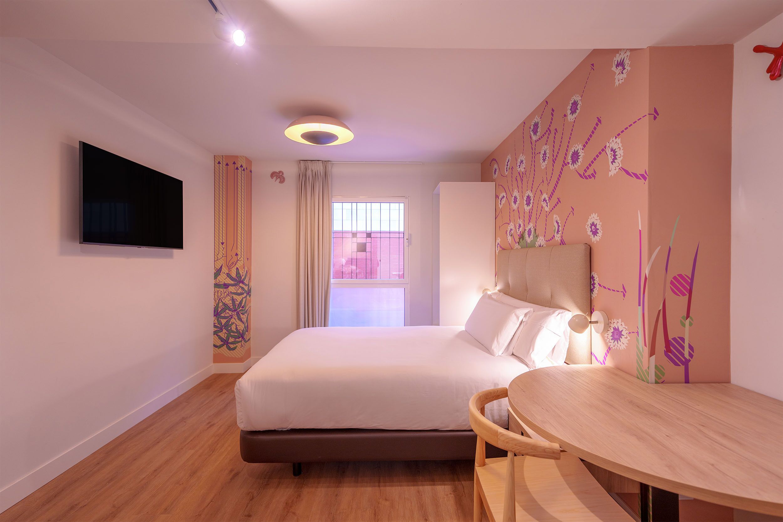 A modern hotel room with a large bed, a flat-screen TV, a wooden table, and a decorative wall.