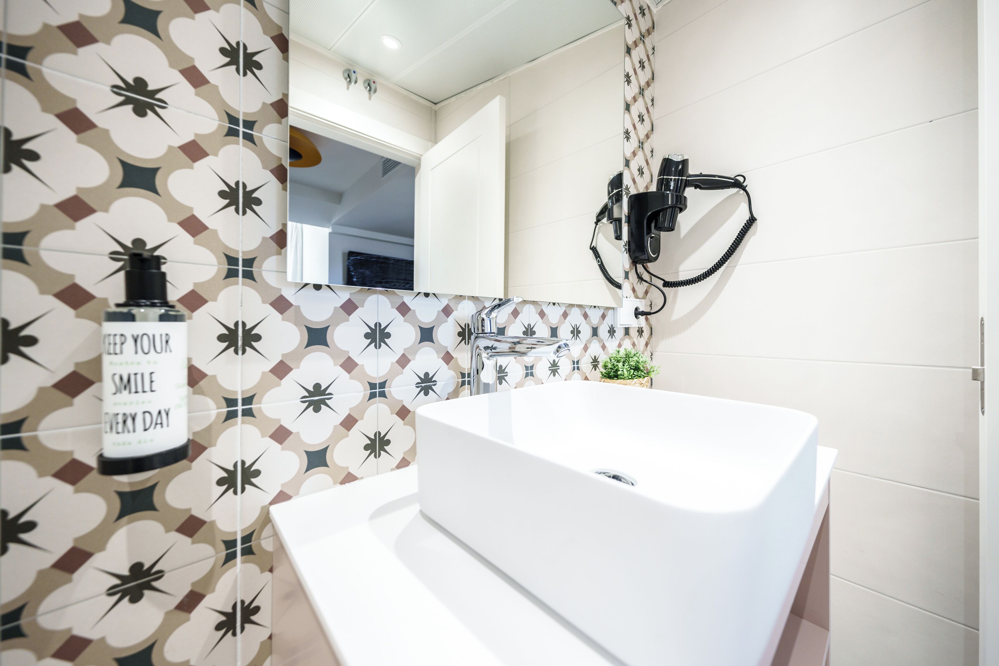 A modern bathroom with a freestanding bathtub, a wall-mounted hairdryer, and a decorative tile backsplash.