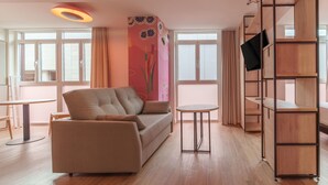 Un salon moderne avec un canapé, une petite table ronde et un téléviseur fixé sur une étagère en bois.
