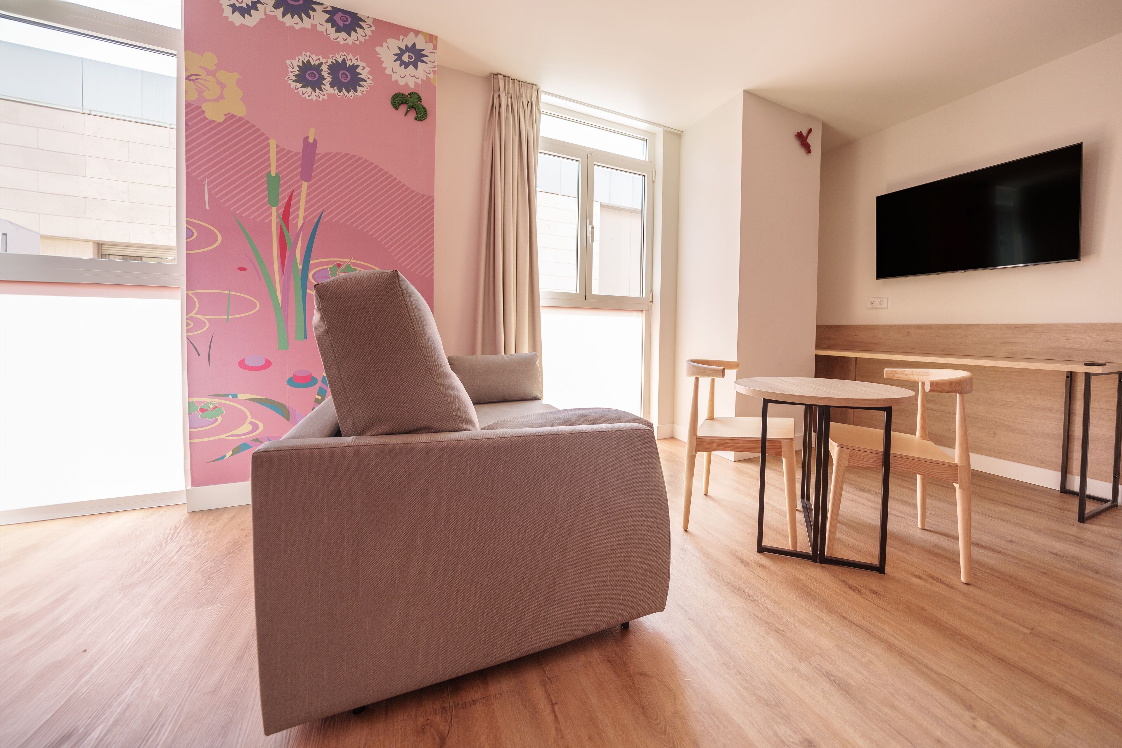 A modern living room with a sofa, a TV mounted on the wall, and a wooden dining table with chairs.