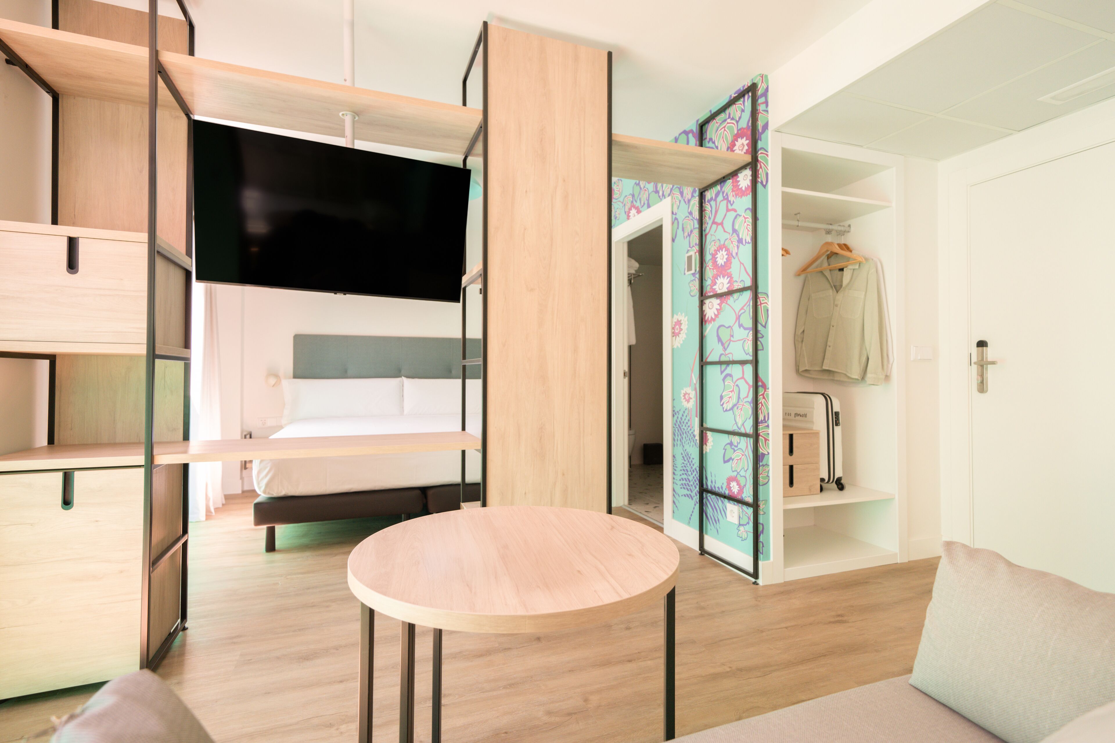 Una habitación de hotel moderna con cama, televisor, mesa redonda y armario abierto.