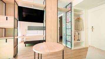 Una habitación de hotel moderna con cama, televisor, mesa redonda y armario abierto.