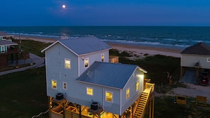 A coastal house with a metal roof, wooden deck, and a staircase leading to the main floor. - Beach Bliss | Epic Views, Games & Pets! (Crystal Beach)