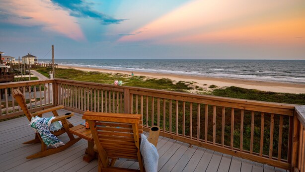 A wooden deck with a rocking chair and a bench overlooking a beach. - Beach Bliss | Epic Views, Games & Pets! (Crystal Beach)