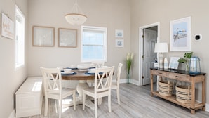 A dining area with a round table, white chairs, a wooden console table with baskets, and framed artwork on the walls. - Beach Bliss | Epic Views, Games & Pets! (Crystal Beach)