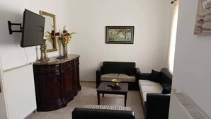 A living room with a dark wooden cabinet, a black sofa, a striped armchair, a coffee table, and a flat-screen TV mounted on the wall. - Marilia House Skiathos (Skiathos)