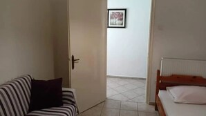 A room with a striped sofa, a bed with a wooden headboard, and a tiled floor. - Marilia House Skiathos (Skiathos)