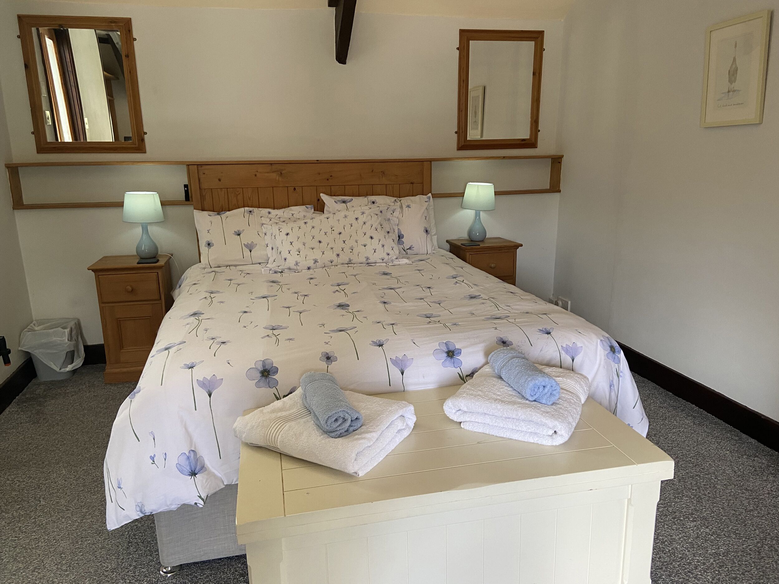 Un letto rifatto con lenzuola a motivi floreali, due abat-jour e un comodino con lampada.