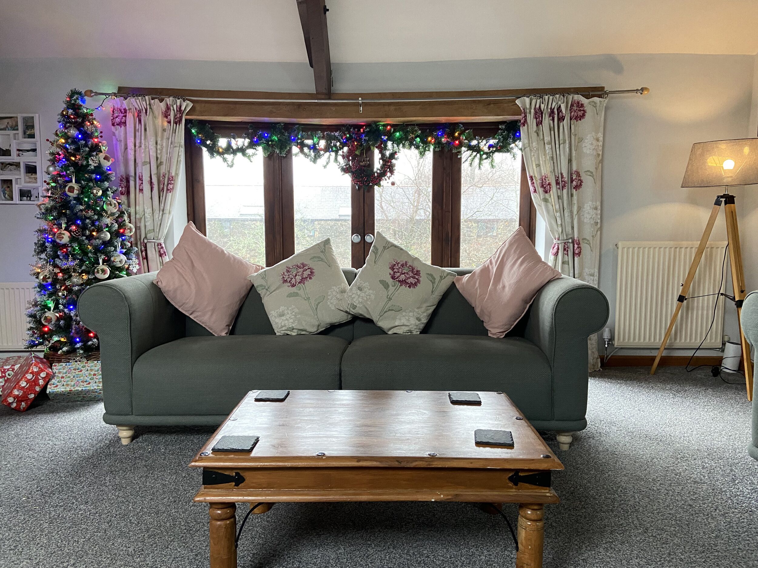 A cozy living room with a green sofa, a wooden coffee table, and a Christmas tree with lights.