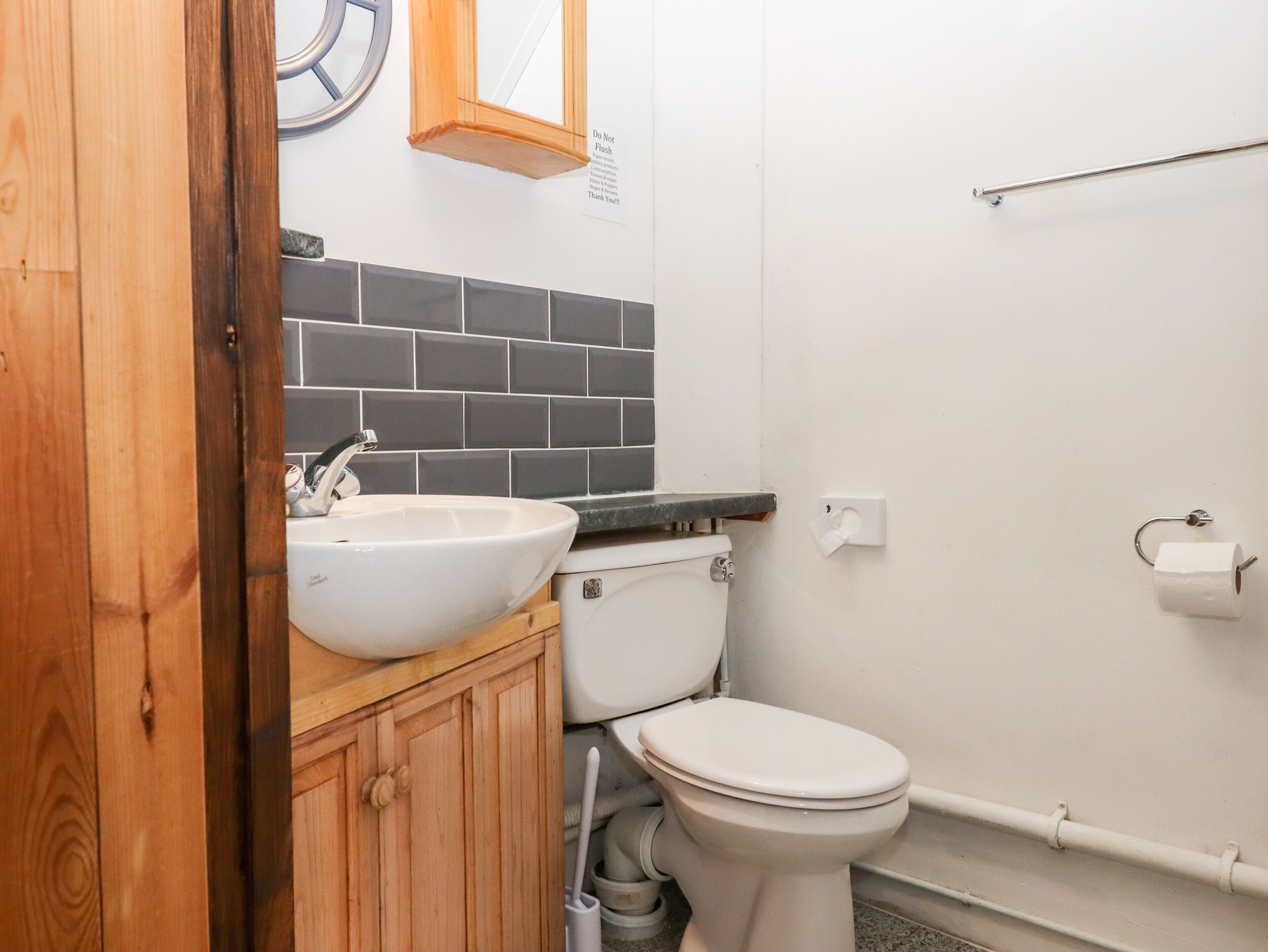 A bathroom with a white sink, wooden cabinet, and a toilet.