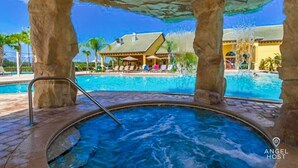 A hot tub area with a pool in the background, stone pillars, and a building with a sloped roof. - Screened Pool & Themed Rooms 8 Miles to Disney (Kissimmee)