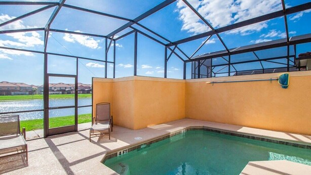 A pool area with a glass enclosure, a chair, and a view of a body of water. - Screened Pool & Themed Rooms 8 Miles to Disney (Kissimmee)
