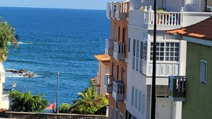 Un carrer costaner amb edificis, una vista despejada del mar i un cotxe estacionat.