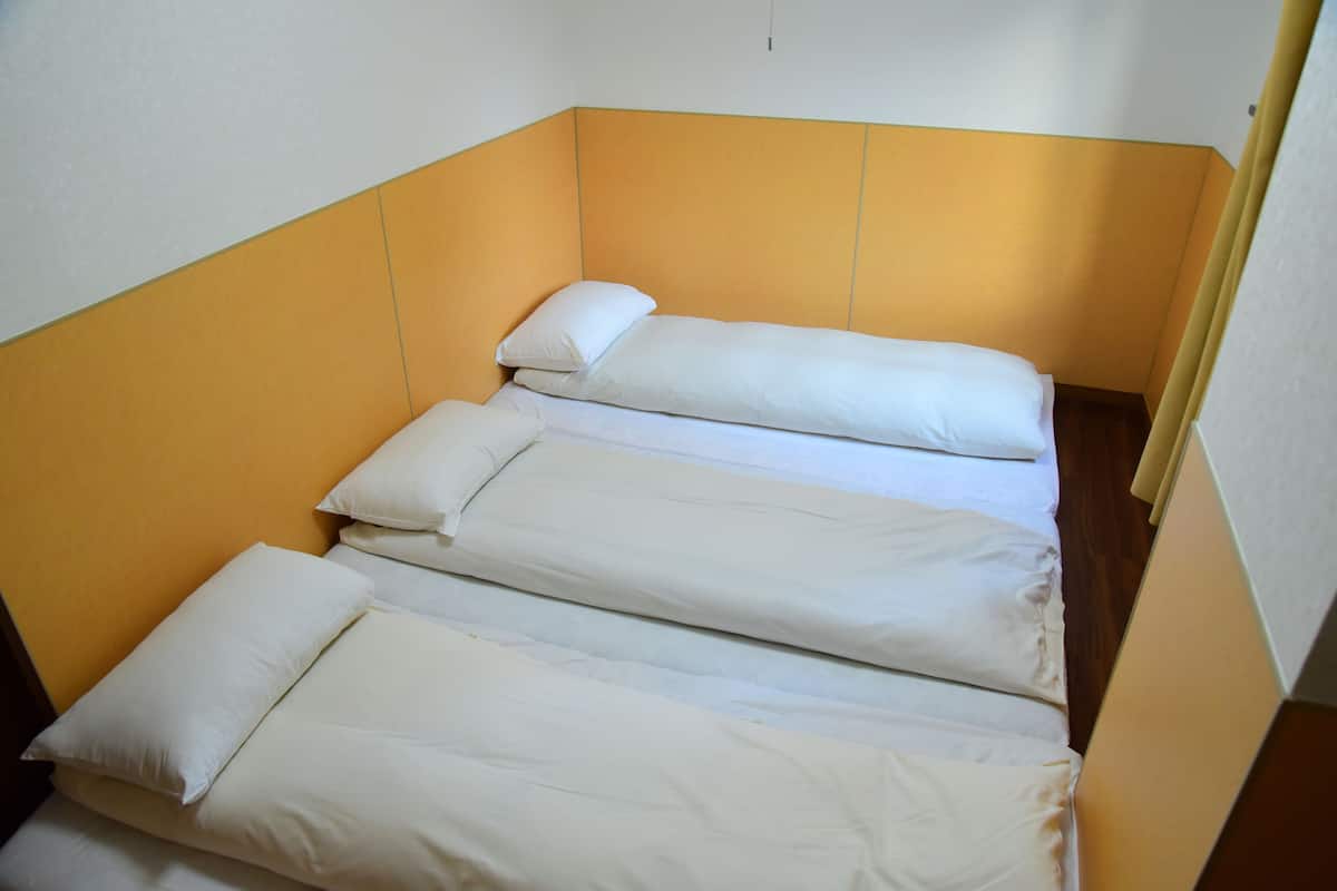 Un lit simple avec une literie blanche, dans une pièce aux murs jaunes et au plancher en bois.