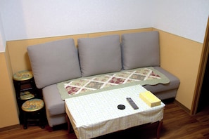 Un canapé d’angle avec une couverture, un petit tabouret et une table sur laquelle se trouvent une télécommande et une boîte.