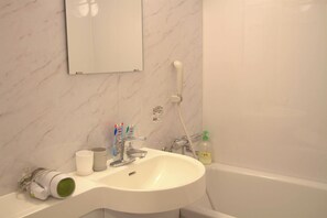 Une salle de bain avec un lavabo blanc, un miroir, une douche et des articles de toilette posés sur le comptoir.