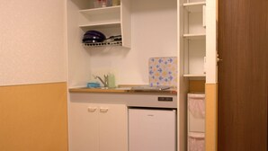 A compact kitchenette with a refrigerator, a sink, and a countertop with a dish rack and a few items. - Ueno House VIP (Tokyo)