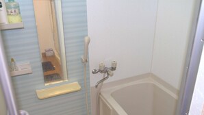 A bathroom with a bathtub, a shower, a mirror, and a shelf with toiletries. - Ueno House VIP (Tokyo)