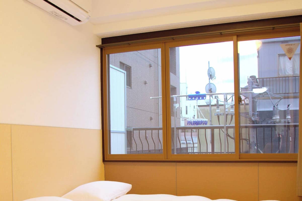 Une chambre d’hôtel avec une grande fenêtre, un lit avec une literie blanche et un climatiseur fixé au mur.