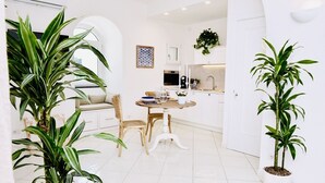 Une cuisine moderne avec des meubles blancs, un coin repas doté d’une table et de chaises en bois, et des plantes en pot.