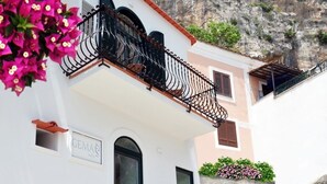 Un bâtiment blanc doté de balcons, une enseigne indiquant « GEMA », et une falaise rocheuse en arrière-plan.
